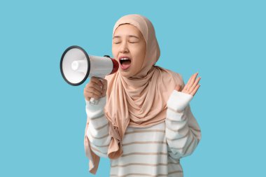Genç Asyalı Müslüman kadın mavi arka planda megafona bağırıyor. Ulusal Duyulma Günü