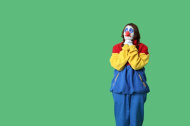 Yeşil arka planda üzgün bir palyaço gibi giyinmiş genç bir kadın. 1 Nisan şakası