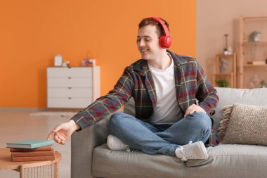 Genç adam sesli kitap dinliyor ve oturma odasında kitap okuyor.