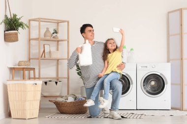 Genç baba çamaşır deterjanıyla selfie çekiyor ve kızı banyoda.