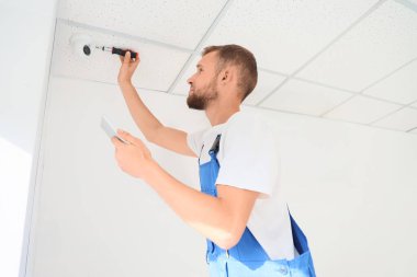 Tablet bilgisayarlı ve tornavidalı erkek işçi odaya alarm sistemi kuruyor