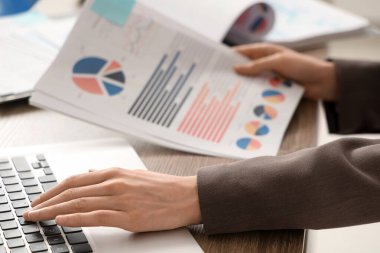 Ofiste dizüstü bilgisayar kullanırken belgelerle çalışan genç bir kadın. Yakın çekim.