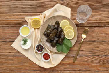 Lezzetli Dolmas tabağı (doldurulmuş üzüm yaprakları), ekşi krema, yağ, baharatlar ve ahşap zemin üzerinde bir bardak su