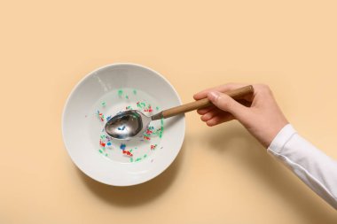 Sarı arka planda plastik ve su dolu bir kadın eli. Mikro Plastik Farkındalık Ayı