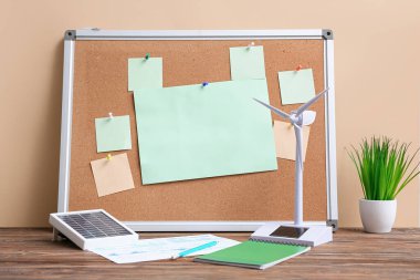 Üzerinde boş kağıtlar ve bej duvarın yanındaki masada rüzgar türbini modeli olan bir pim tahtası. Yeşil Enerji kavramı