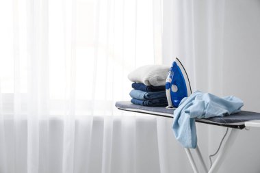 Odanın penceresinin yanında elektrikli ütü ve giysi bulunan tahta.