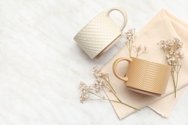 Kurumuş çiçekli farklı seramik bardaklar ve açık arkaplanda peçete.