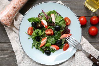 Yengeç çubuklu bir tabak salata, ıspanak, siyah zeytin ve ahşap zemin üzerinde domates.