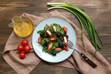 Yengeç çubuklu bir tabak salata, ıspanak, siyah zeytin ve ahşap zemin üzerinde domates.