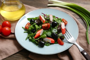 Yengeç çubuklu bir tabak salata, ıspanak, siyah zeytin ve ahşap zemin üzerinde domates.