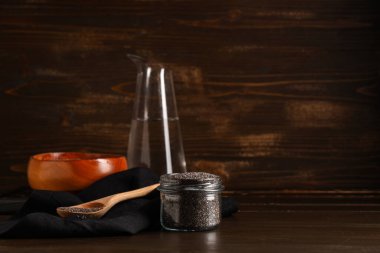 Ahşap zemin üzerinde chia tohumları olan kavanoz ve kaşık.