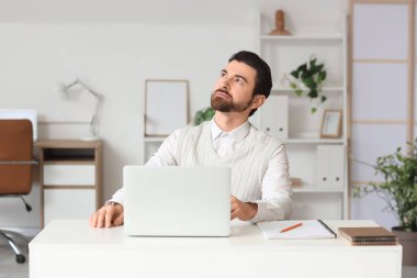 Dizüstü bilgisayarı olan genç adam masadaki masaya doğru bakıyor.