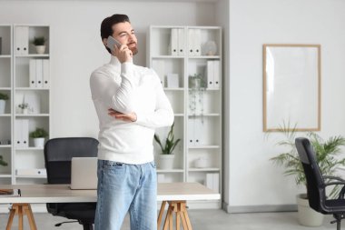 Genç adam ofiste cep telefonuyla konuşuyor.