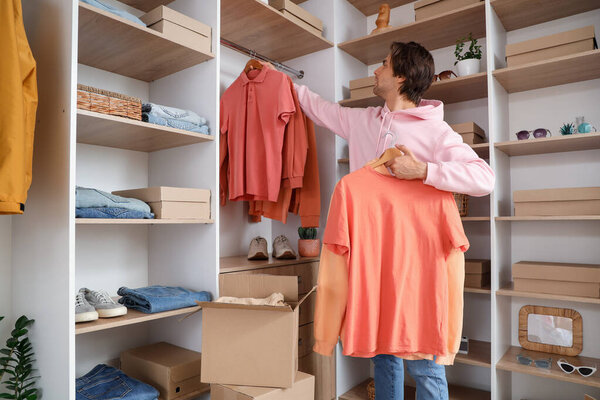 Handsome young man arranging stylish clothes in dressing room