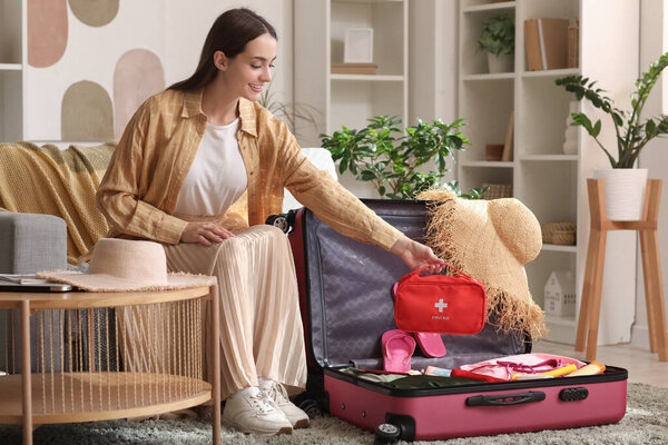 Молодая счастливая женщина с чемоданом и аптечкой сидит дома на диване. Концепция путешествия