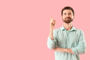 Yakışıklı adam pembe arka plandaki bir şeyi işaret ediyor.