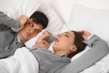 Karısının evde yüksek sesle horlamasından rahatsız olan genç bir adam.