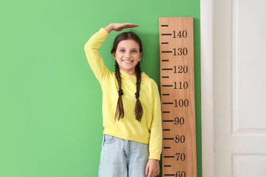 Yeşil duvarın yanında boyunu ölçen tatlı bir kız.