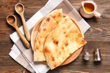 Ahşap zemin üzerinde lezzetli lavaş, kaşık ve bir sürahi yağ olan tabaklar.