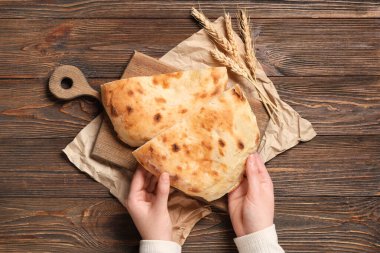 Lezzetli lavaş parçaları ve ahşap arka planda buğday dikenli kadın elleri.