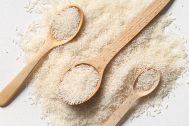 Beyaz arka planda çiğ pirinçli tahta kaşıklar.