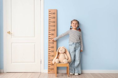 Evdeki stadyumun yanındaki sandalyede boyunu ölçen küçük kız.