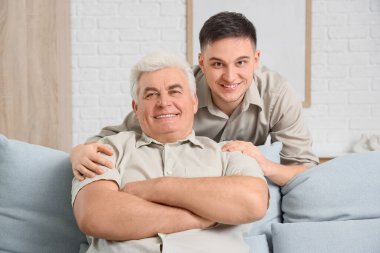 Evdeki kanepede babasına sarılan genç adam.