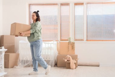 Taşındığı gün çocukların yatak odasında karton kutu taşıyan hamile bir kadın.