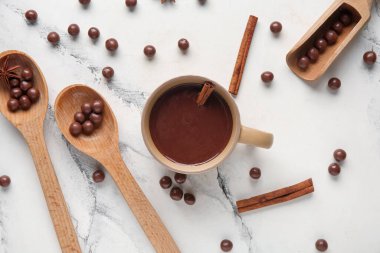 Bir fincan sıcak çikolata, tahta kaşıklar, toplar ve mermer arka planda tarçın çubukları.