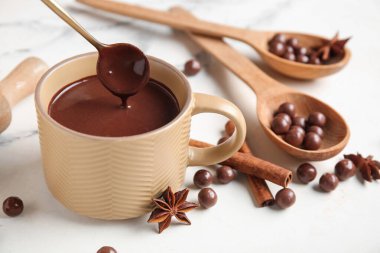 Bir fincan sıcak çikolata, kaşık, toplar ve mermer arka planda tarçın çubukları