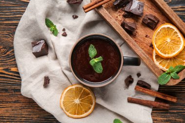 Bir fincan naneli çikolata, kurutulmuş portakal dilimleri ve ahşap arka planda tarçın çubukları.