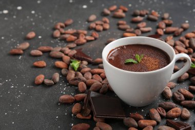 Nane yapraklı bir fincan sıcak çikolata ve siyah grunge arka planda kakao çekirdeği.