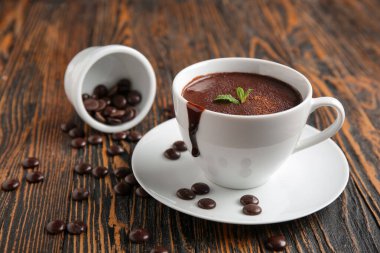 Tahta zemin üzerinde cips ve nane yaprağı olan bir fincan sıcak çikolata.