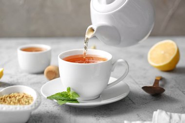 Gri arka planda fincana sıcak karabuğday çayı dökülüyor.