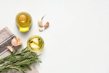 Beyaz arka planda biberiyeli taze sarımsak yağı şişesi ve cam kase.