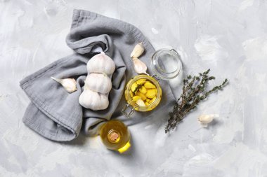 Kavanoz ve bir şişe taze sarımsak yağı ve gri arka planda kekik.