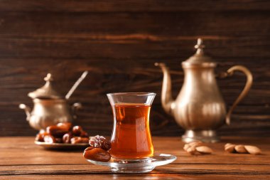 Çaydanlıklı bir bardak Türk çayı, ahşap zemin üzerinde kurumuş hurma ve badem.