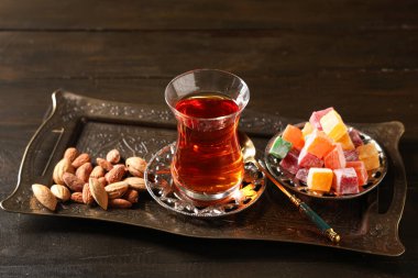 Bir bardak Türk çayı, ahşap zemin üzerindeki tatlar ve bademlerle dolu tepsi