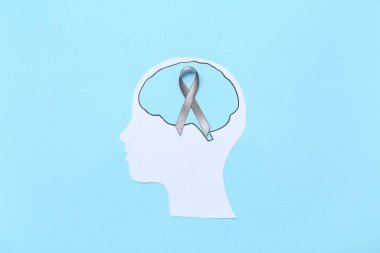 Beyni ve mavi arka planda gri farkındalık kurdelesi olan kağıt insan kafası. Kanser kavramı