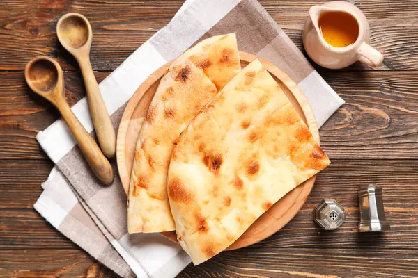 Ahşap zemin üzerinde lezzetli lavaş, kaşık ve bir sürahi yağ olan tabaklar.