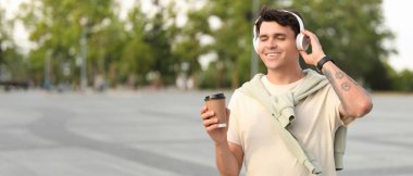 Bir fincan kahveyle yakışıklı genç adam açık havada müzik dinliyor.