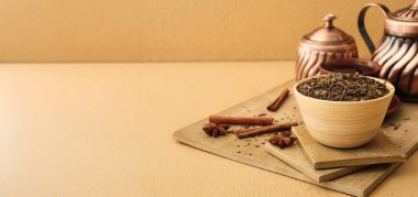 Kuru çay yaprakları ve bej arkaplandaki baharatlarla dolu bir kase.