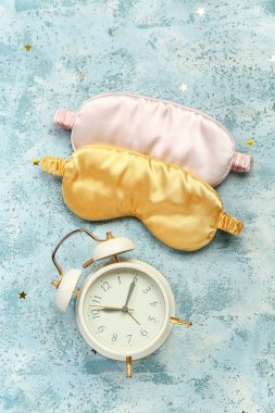 Sleeping masks and alarm clock on color background. World Sleep Day concept