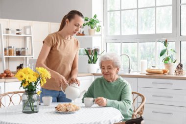 Genç bir kadın mutfakta büyükannesi için fincana çay dolduruyor.