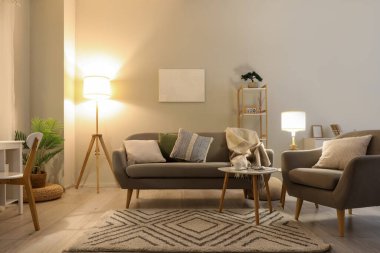 Oturma odasının içinde rahat gri kanepe, koltuk ve parlak lambalar.