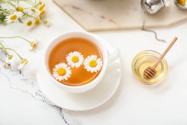 Beyaz mermer arka planda bir fincan sıcak papatya çayı ve bal.