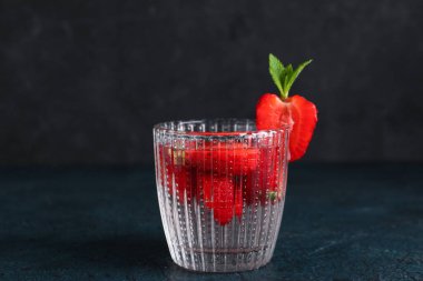 Siyah arka planda çilekli bir bardak erimiş su.