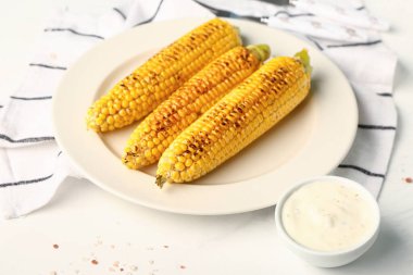Lezzetli ızgara mısır koçanı ve beyaz arka planda sos tabağı.