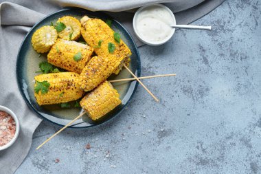 Lezzetli ızgara mısır koçanı şiş ve mavi arka planda maydanoz tabağı.