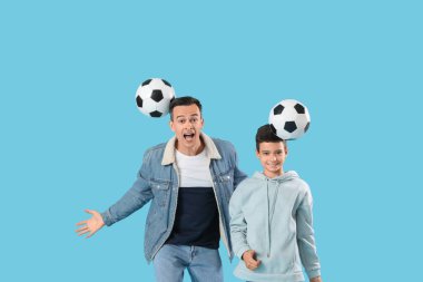 Küçük çocuk ve babası mavi arka planda futbol toplarıyla oynuyorlar.